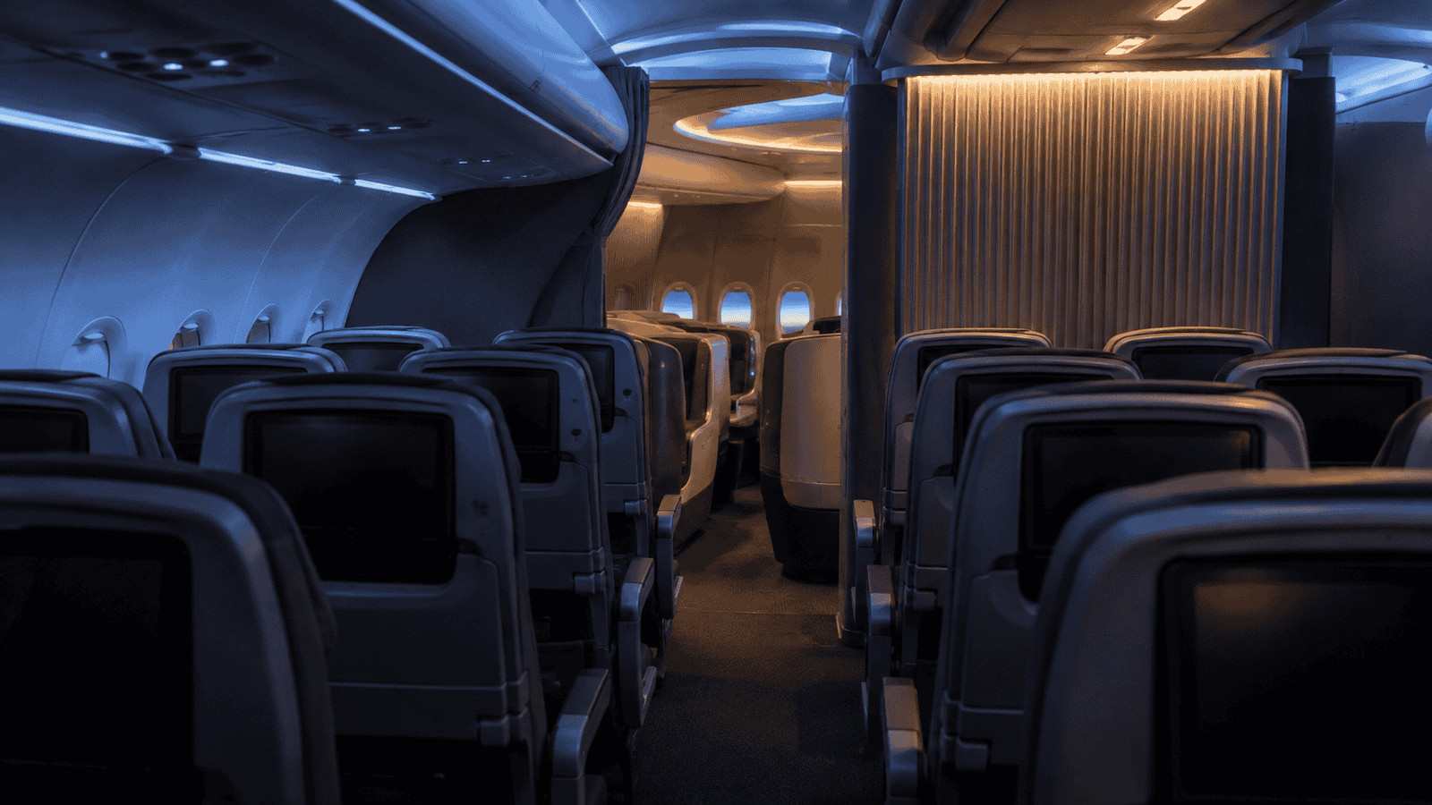 Economy cabin seats leading toward a quieter premium cabin area with blue and amber lighting